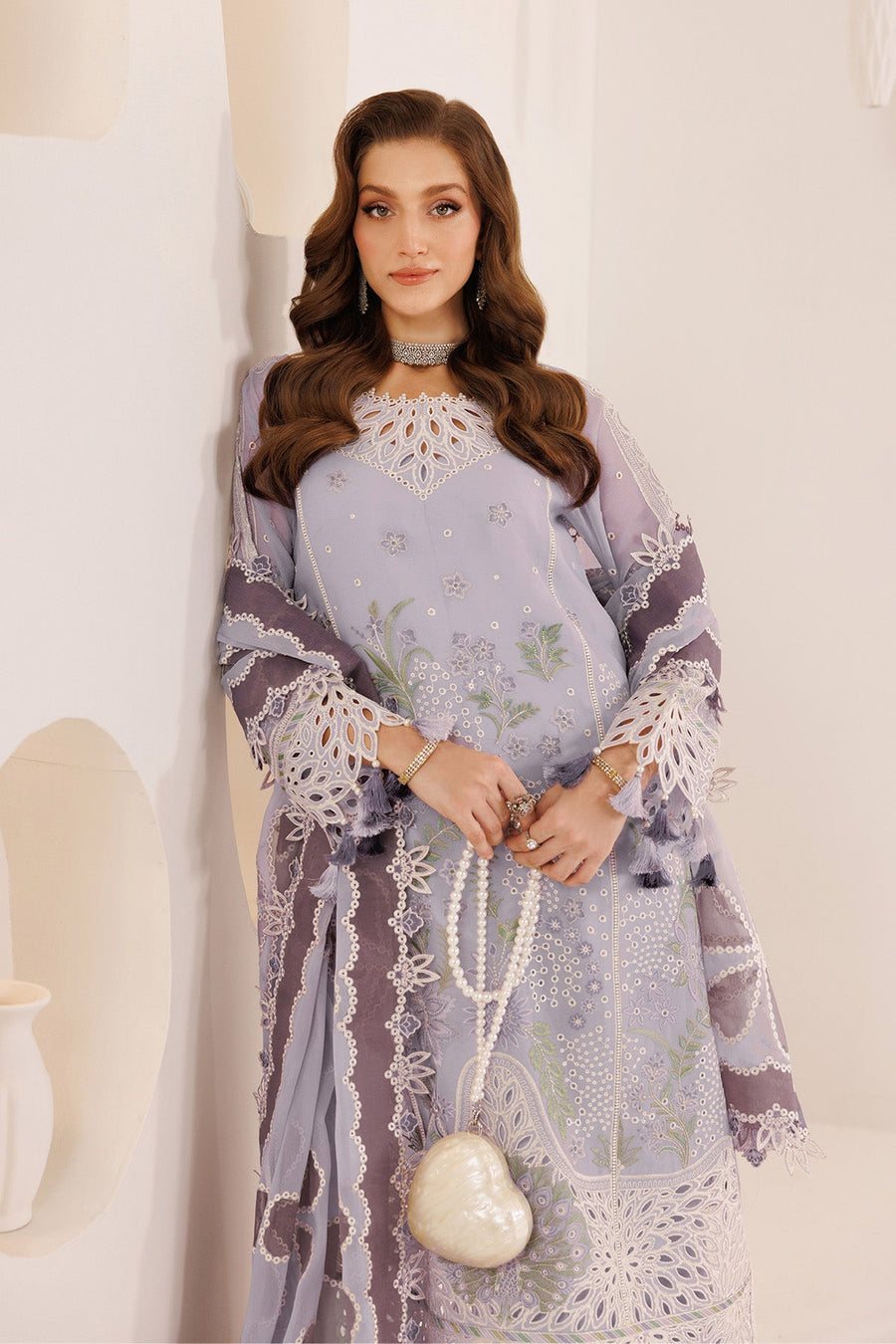 Woman posing with pearl necklace accessory in elegant lavender suit with floral motifs
