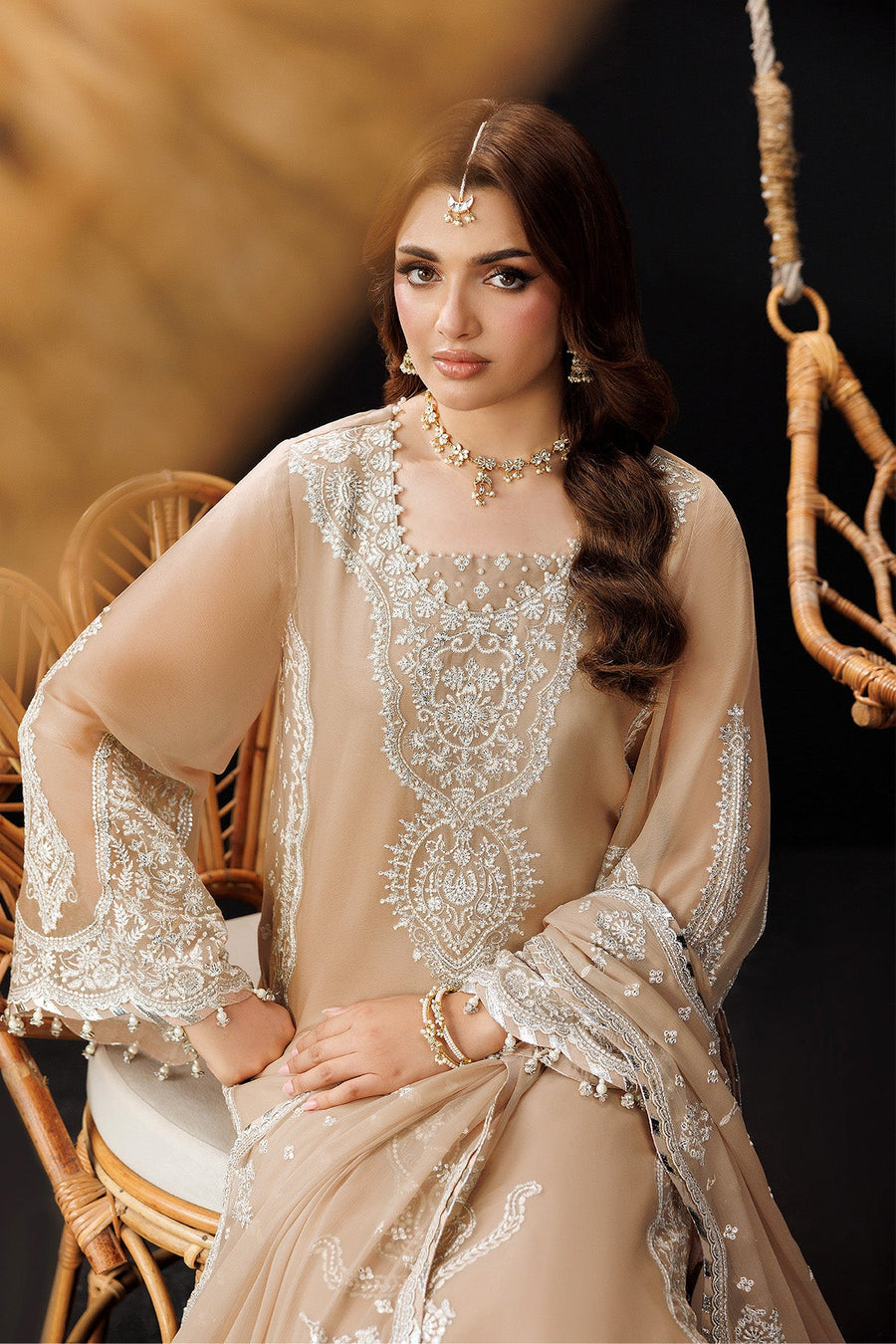 Model sitting on a chair showcasing full outfit and embroidered details on sleeves and hem