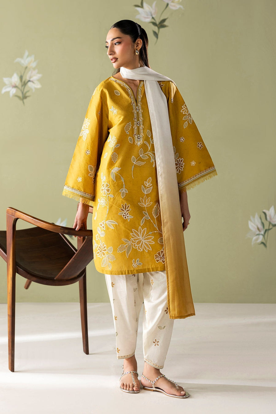 Close-up of model looking downward showcasing delicate gold floral earrings and rings with embroidery details on shirt sleeve
