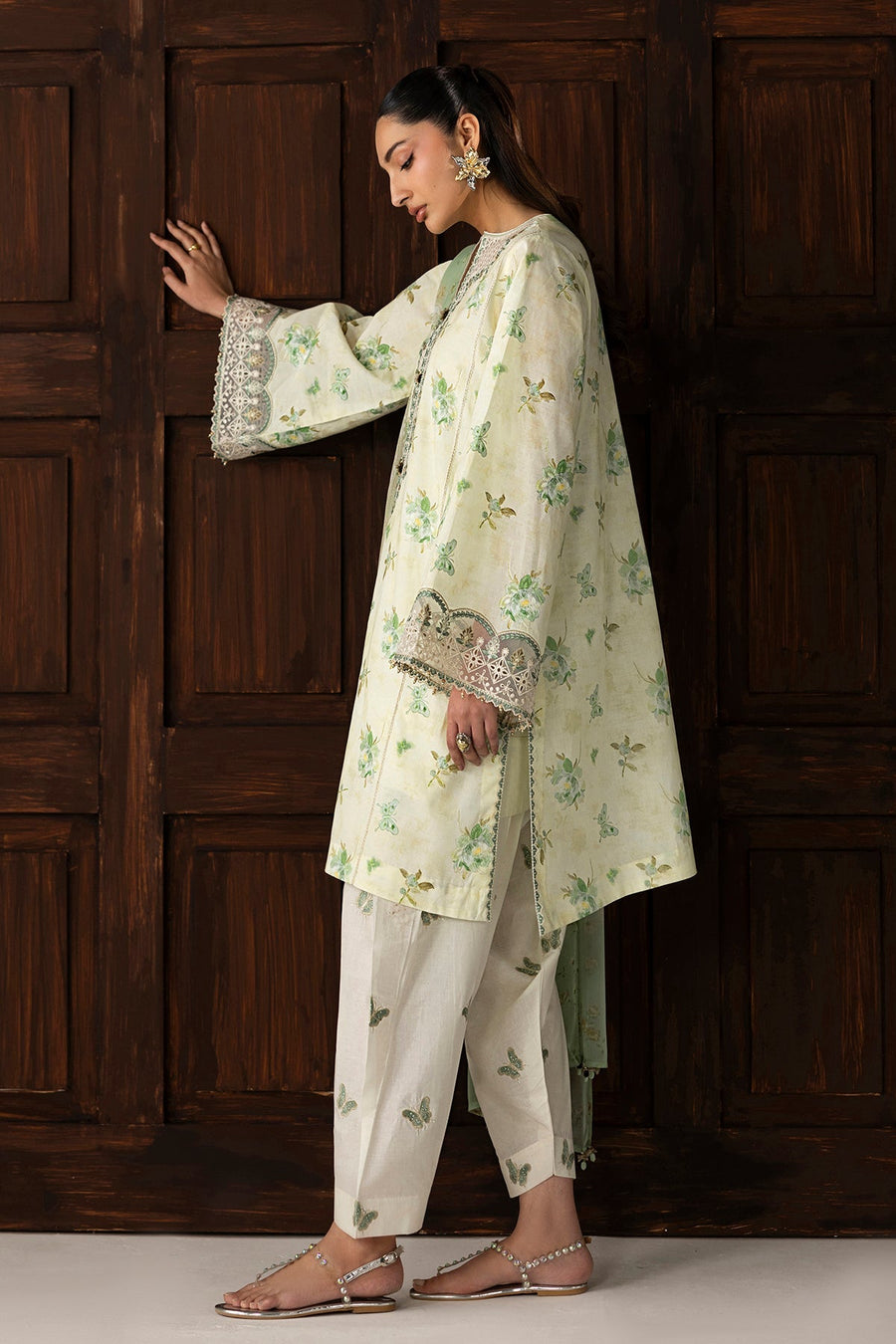 Side view of model wearing embroidered lawn suit with butterfly-printed pants and sheer dupatta