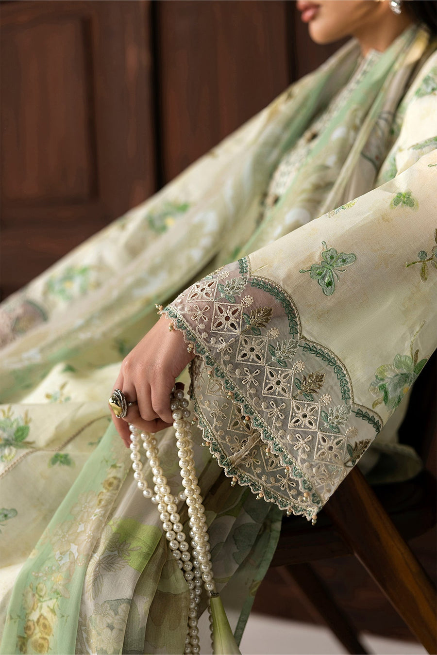 Close-up of intricate lace embroidery and beadwork on sleeve cuff holding pearl accessory
