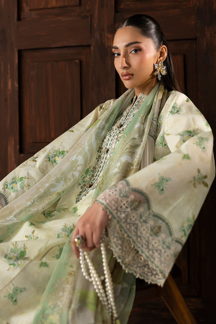Model sitting on chair wearing embroidered lawn suit showing floral printed dupatta and pants