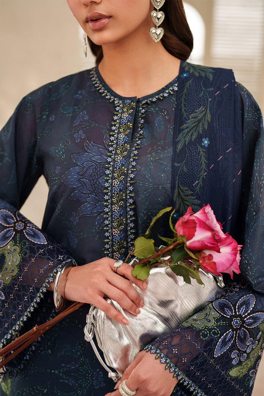 Front view of woman wearing navy embroidered lawn suit holding a bunch of pink roses