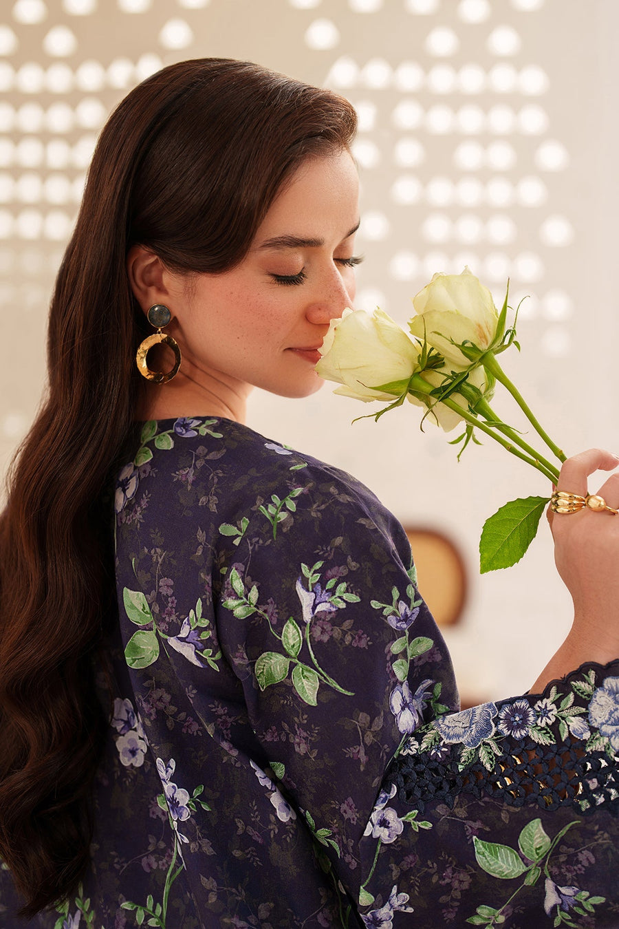 Close-up of woman smelling white roses, wearing a navy floral embroidered kurta with detailed embroidery on sleeves, accessorized with gold jewelry.
