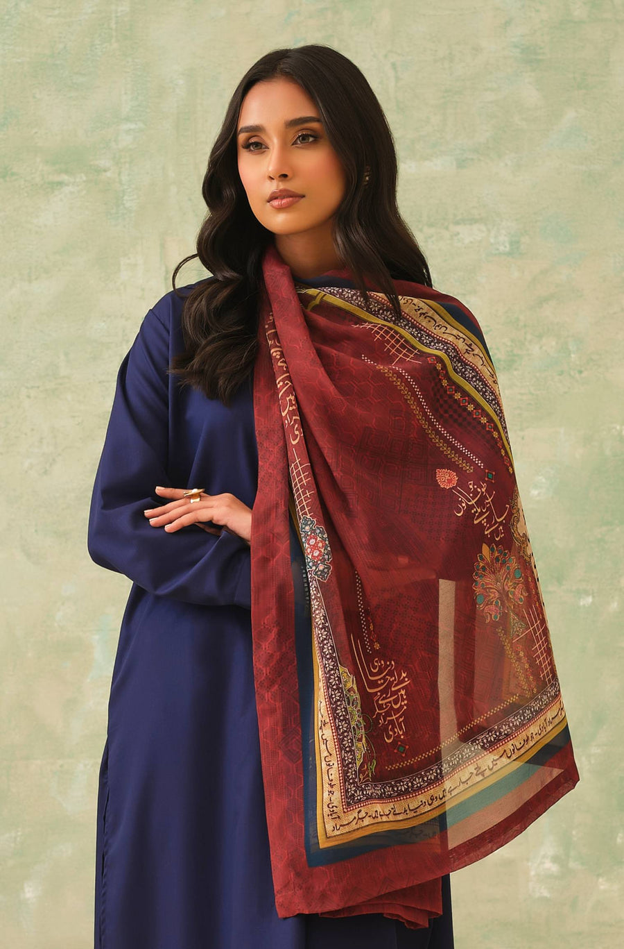 Woman wearing a rust-colored embroidered and printed Swiss lawn dupatta with intricate Urdu calligraphy and ornamental patterns over a navy blue outfit