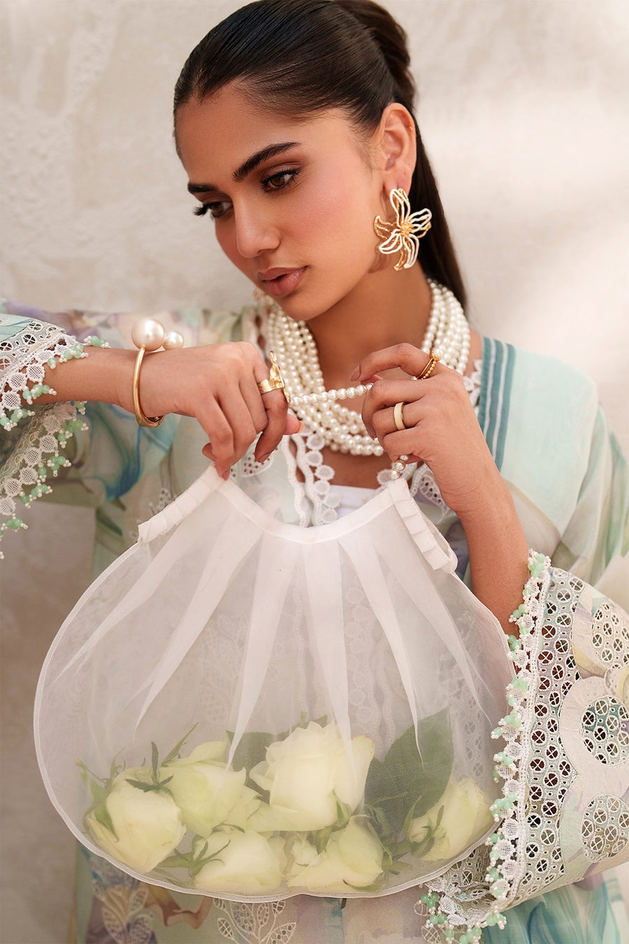 Model wearing full pastel green embroidered lawn ensemble accessorized with pearl jewelry and sheer floral dupatta indoors by window