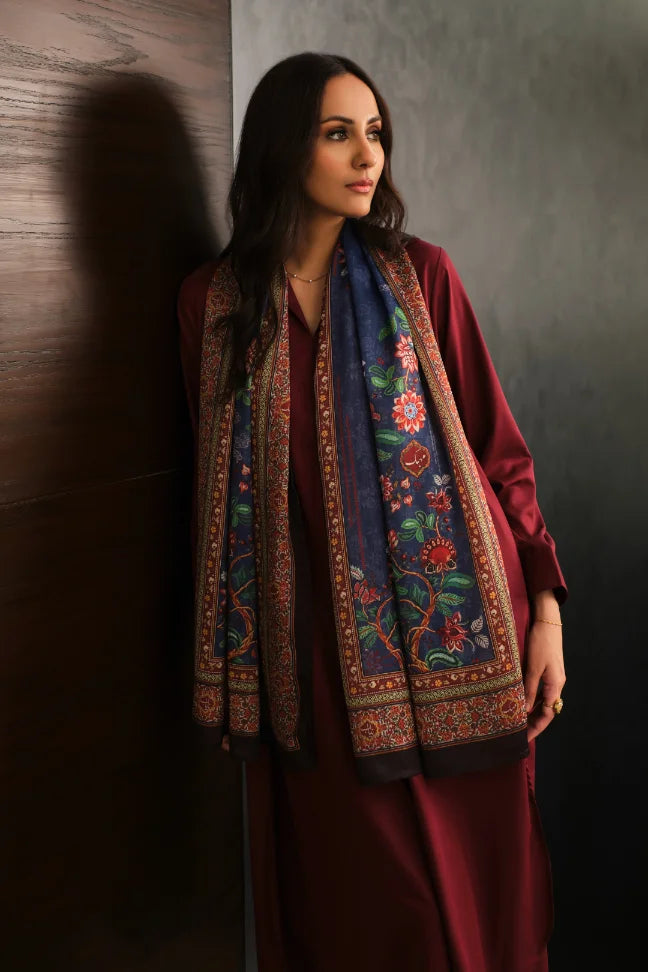Woman wearing a navy embroidered floral scarf over a maroon dress standing against a dark wall