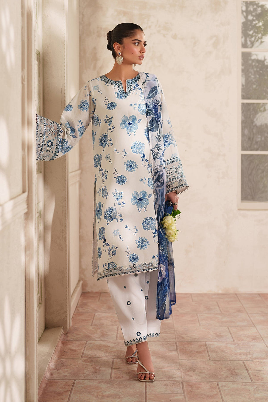 Close-up focusing on white roses and blue clutch in hand against embroidered cuff of lawn suit.