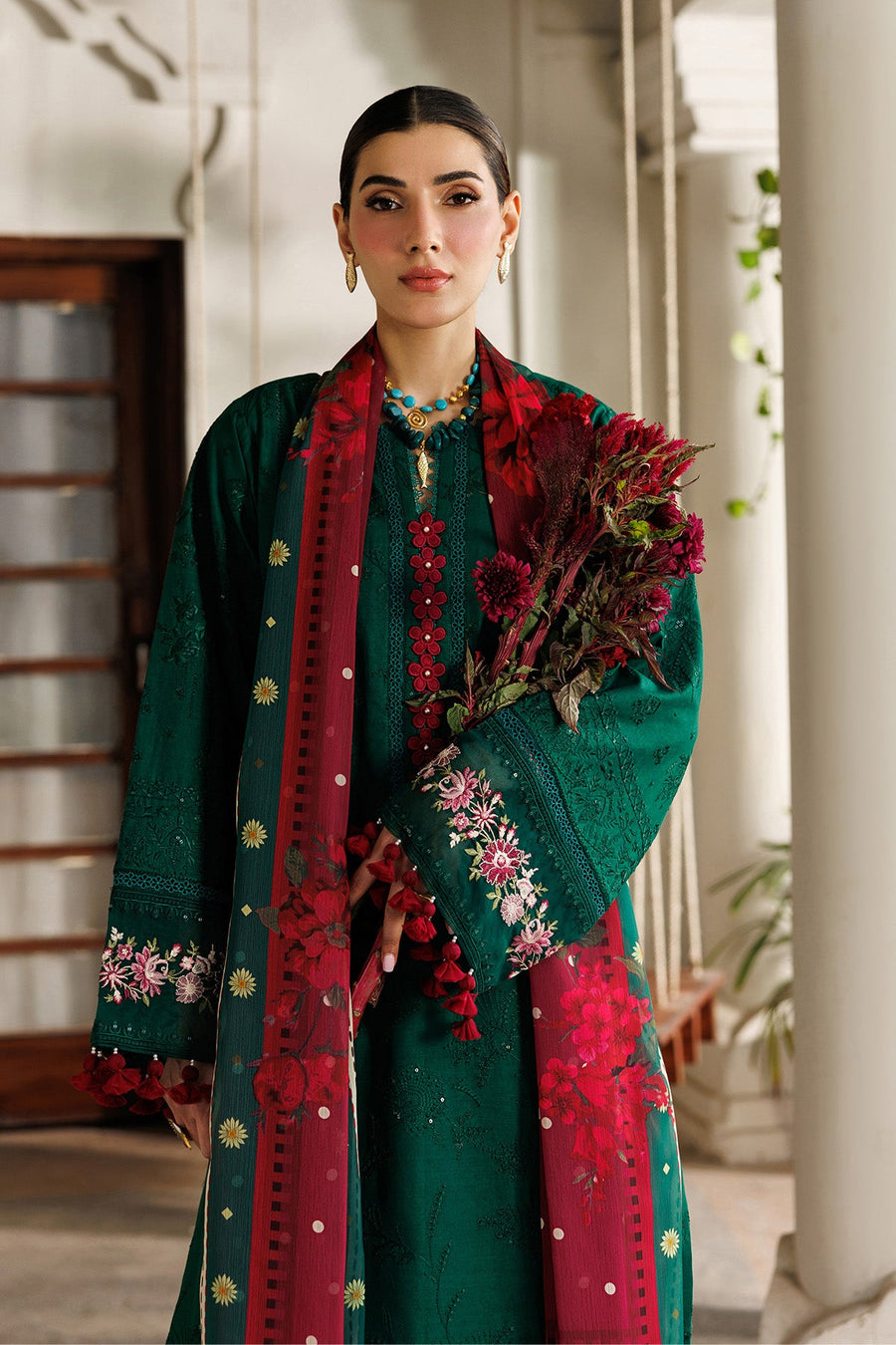 Side view of model holding embroidered lawn suit bouquet with red floral accessories