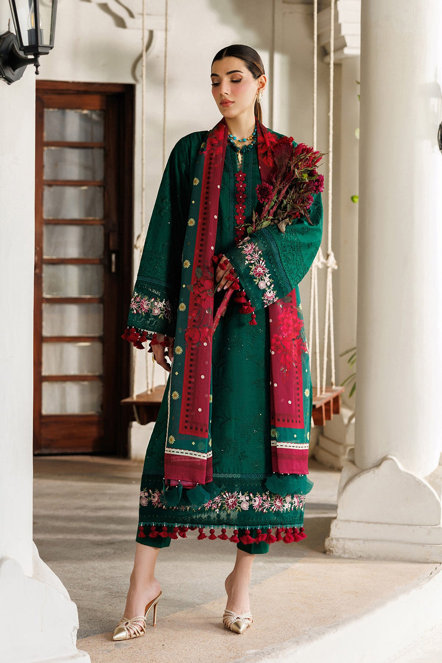 Woman posing indoors in embroidered emerald green lawn suit featuring intricate front embroidery and tassels