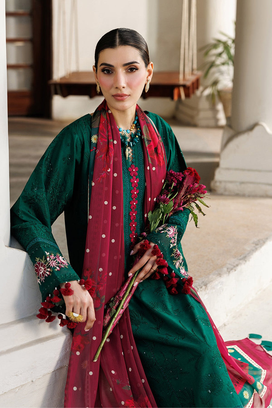 Woman seated wearing embroidered lawn suit with detailed embroidery and floral dupatta draped gracefully