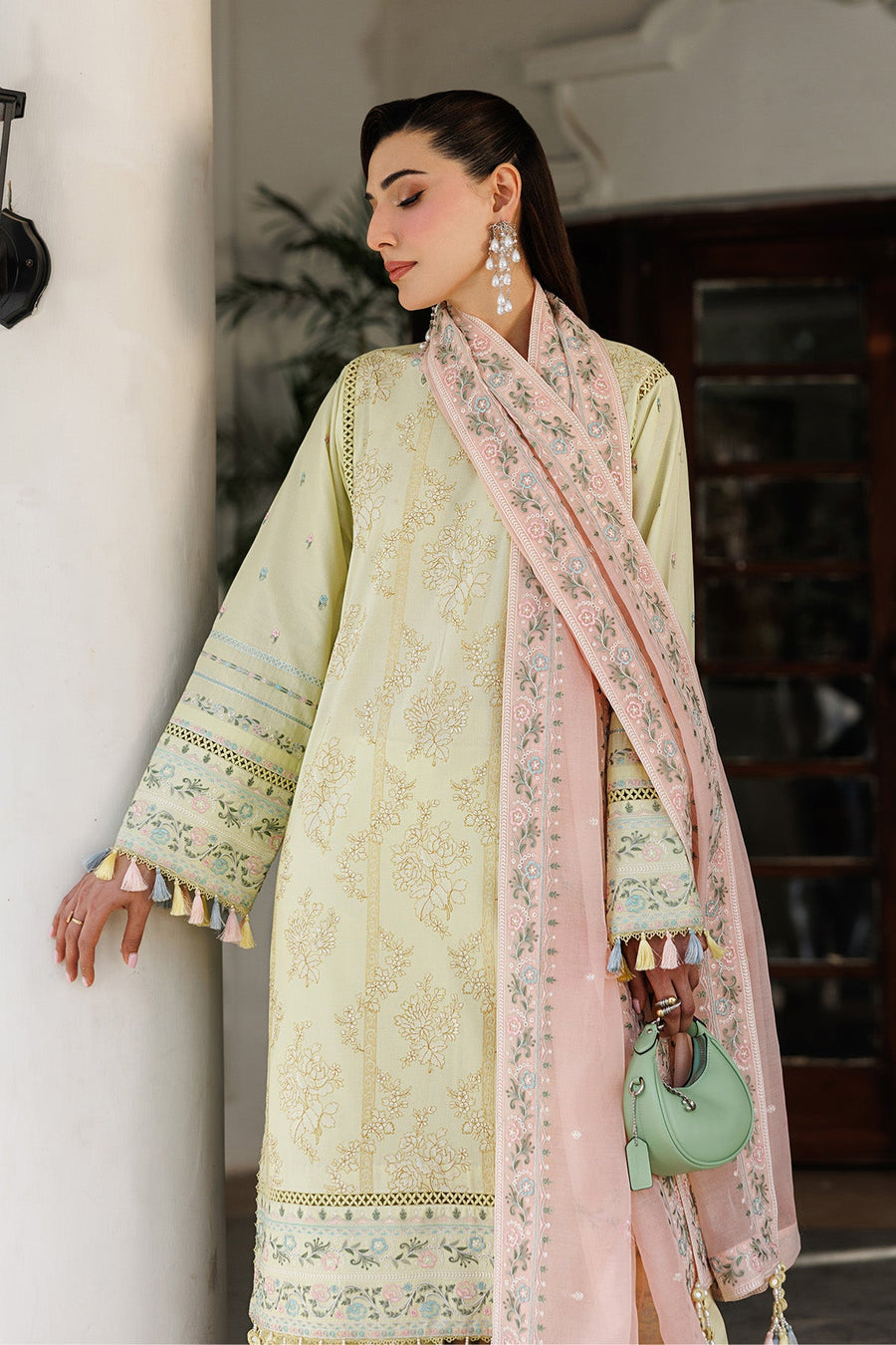 Side view of embroidered yellow lawn shirt hem with multicolor tassels above matching trousers