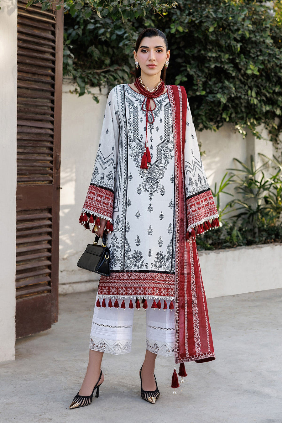 Woman wearing embroidered white lawn suit with black and red detailed patterns, holding black handbag