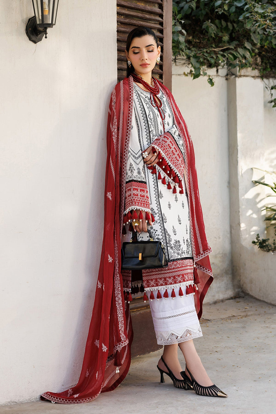 Close-up of woman's upper body showcasing intricate black embroidery on white lawn fabric and red tassels