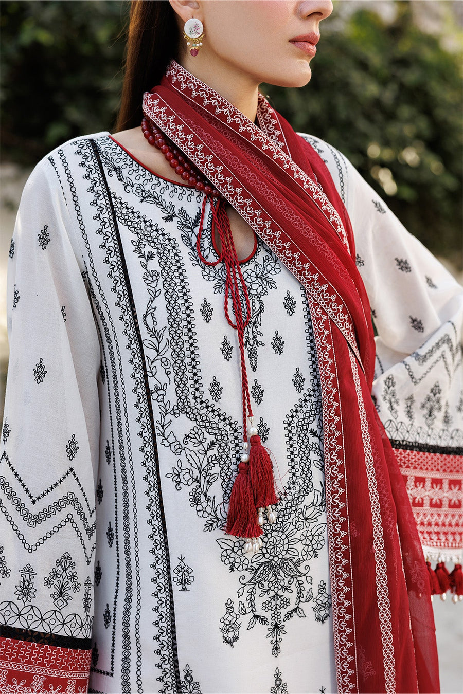 Close-up of detailed embroidery and tassels on white lawn fabric with black and red design