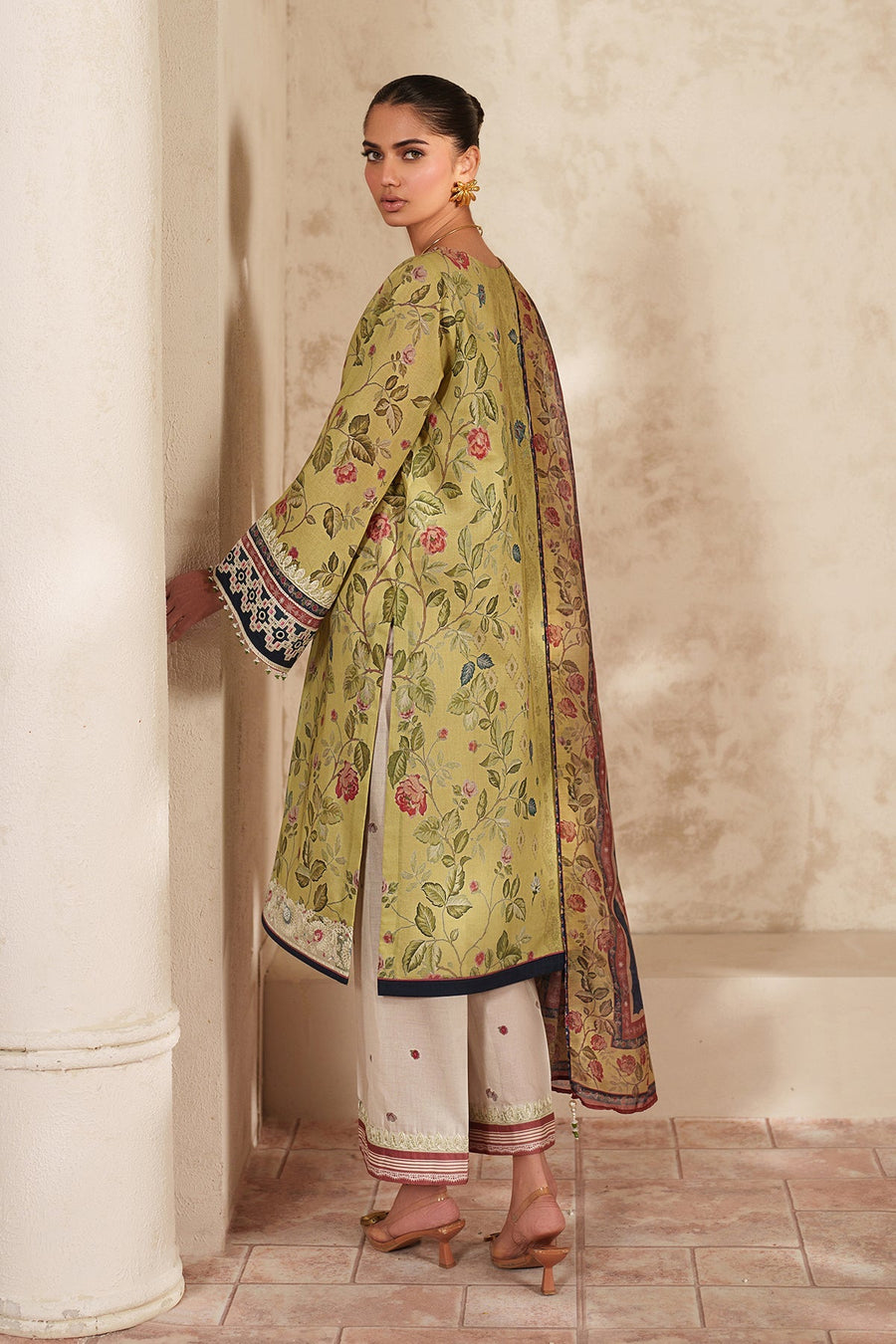 Back view of a woman in a long soft green floral embroidered lawn shirt paired with white pants showing detailed embroidery on sleeves and hem