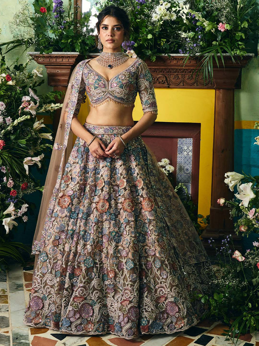 Woman wearing an exquisitely embroidered floral lehenga with deep V-neck choli and matching dupatta, standing in a floral decorated room.