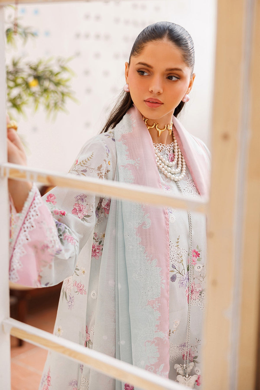 Two women seated featuring different pastel floral embroidered lawn suits with matching embellished dupattas and elegant jewelry