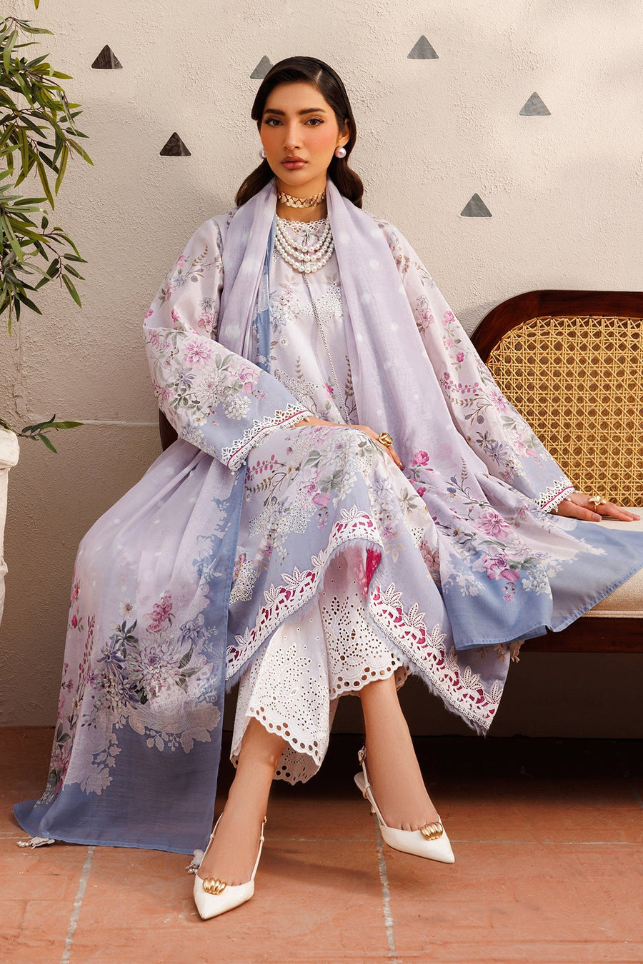 Close-up side profile of woman in embroidered suit sitting near a wicker chair, showcasing detailed floral patterns and accessories.