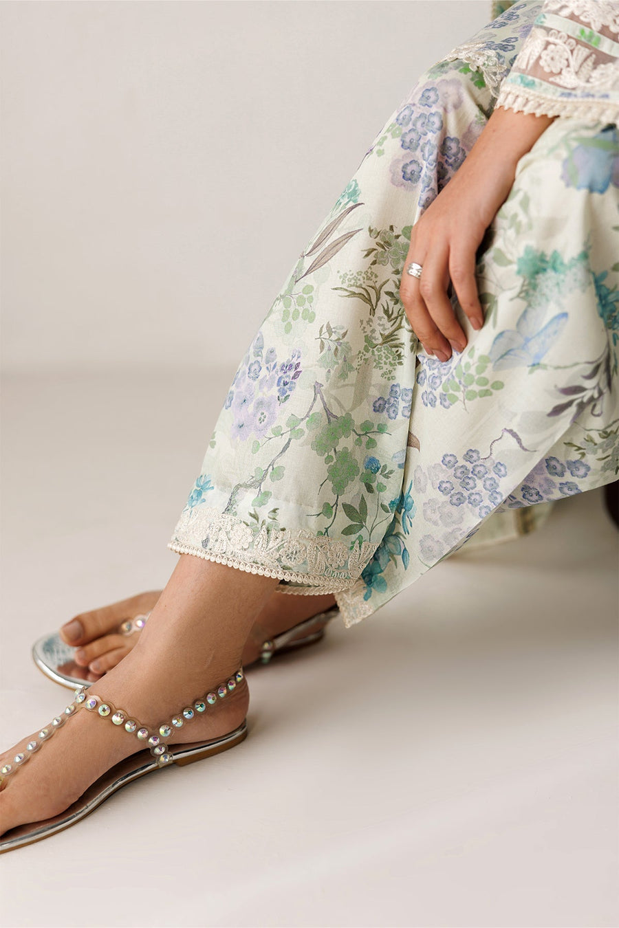 Close-up of trousers’ hem with intricate lace detailing paired with jeweled sandals