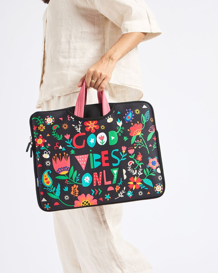 Woman holding a black laptop sleeve with colorful floral prints and 'Good Vibes Only' text, featuring pink handles