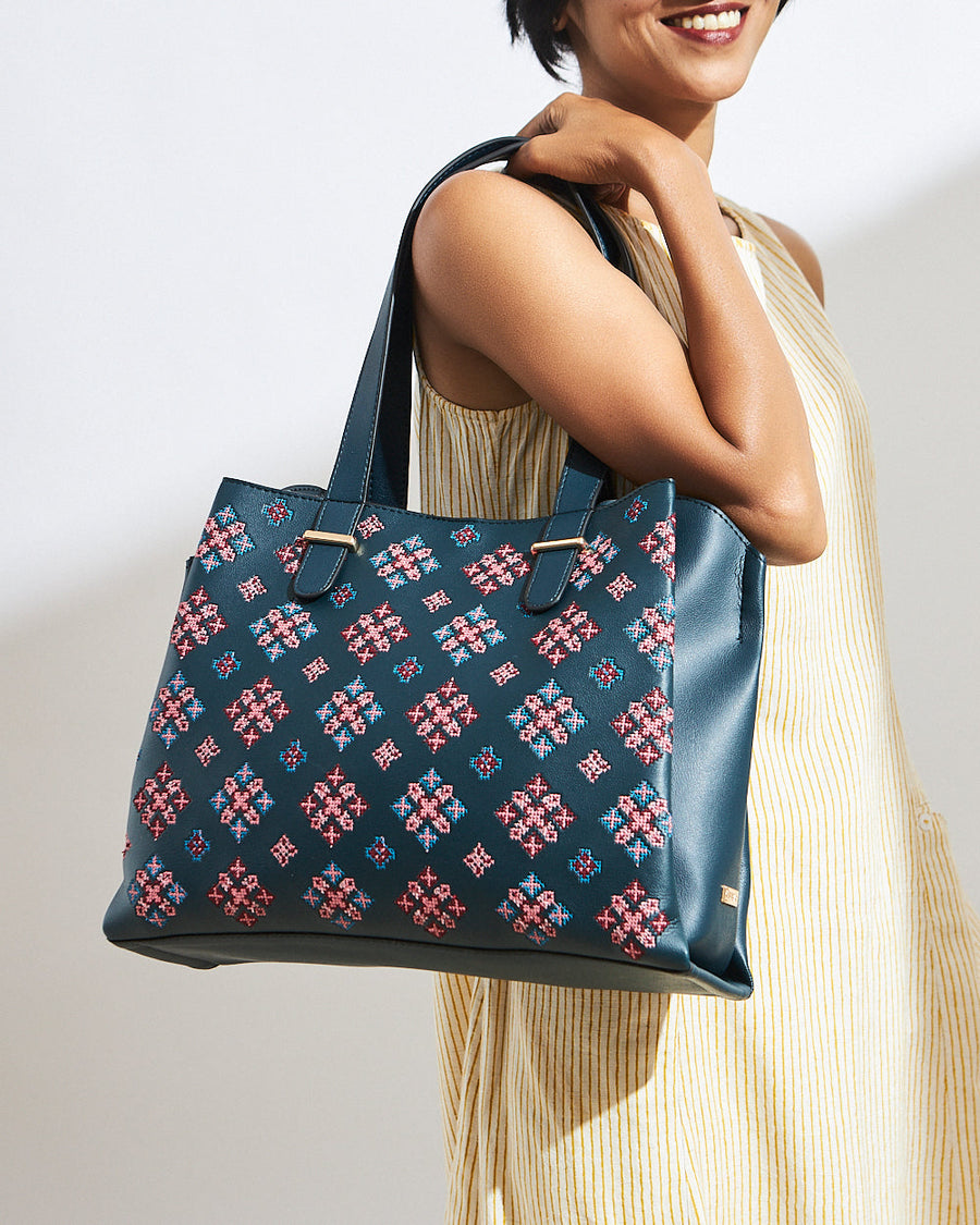 Woman holding an elegant deep teal vegan leather tote with colorful geometric embroidery over shoulder