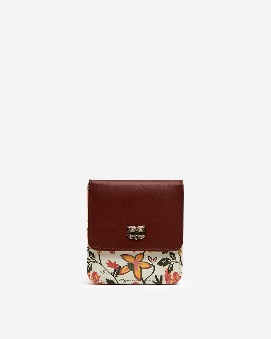 Front view of a compact women's wallet with a brown leather flap and vibrant floral print, featuring a decorative owl emblem