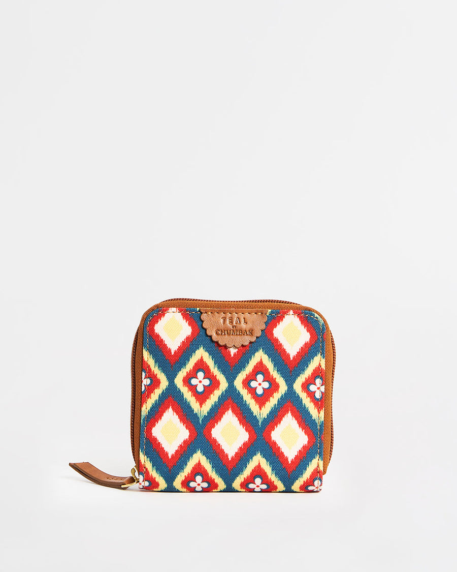 Front view of a compact mini wallet with vibrant ikkat diamond pattern in red, blue, yellow, and cream, featuring a zipper closure and brown PU leather accents.