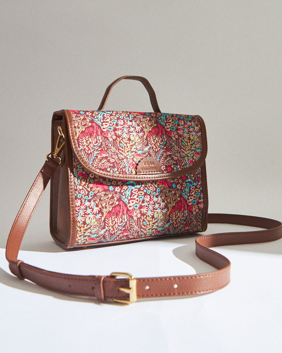 Elegant crossbody bag with floral embroidery on fabric body and brown leather adjustable strap and handle