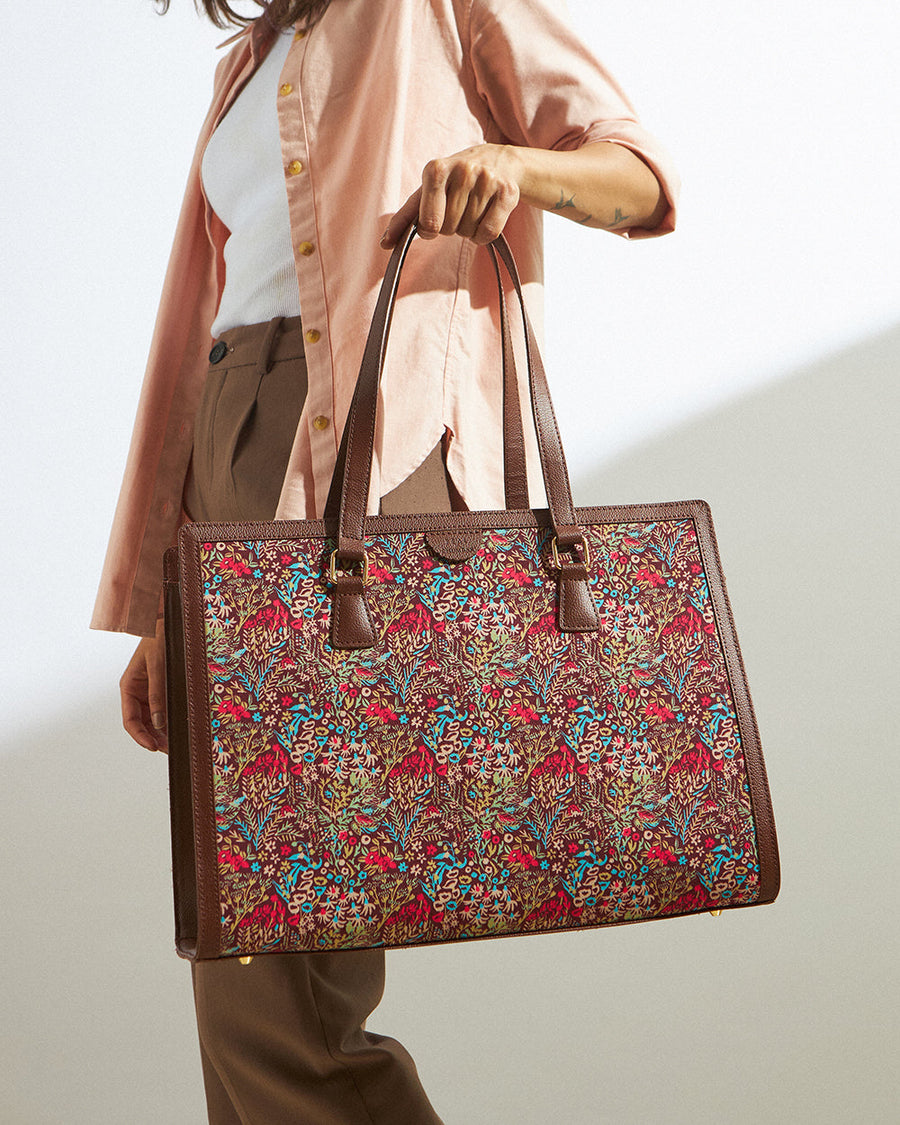 Woman holding a floral patterned tote bag with brown vegan leather handles, dressed in neutral shirt and pants