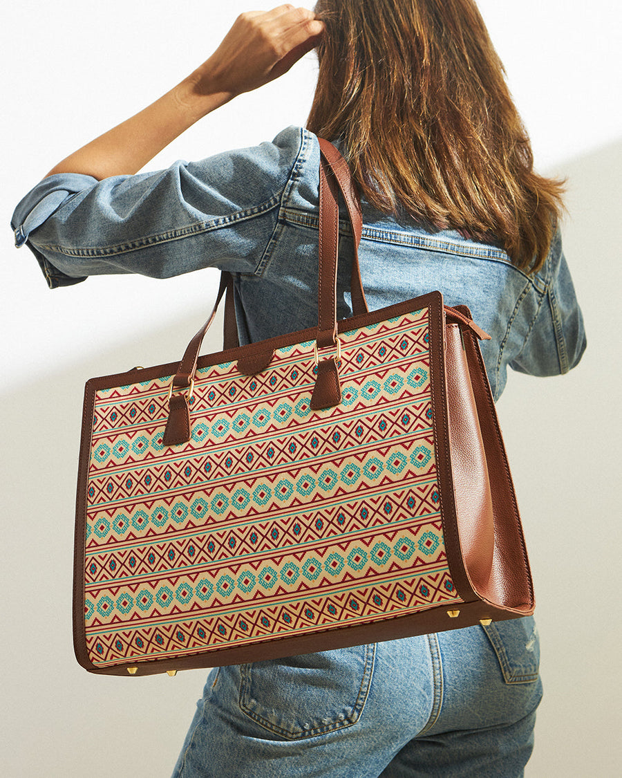 Woman carrying an Aztec patterned office tote with brown vegan leather handles over her shoulder while wearing a denim jacket and jeans