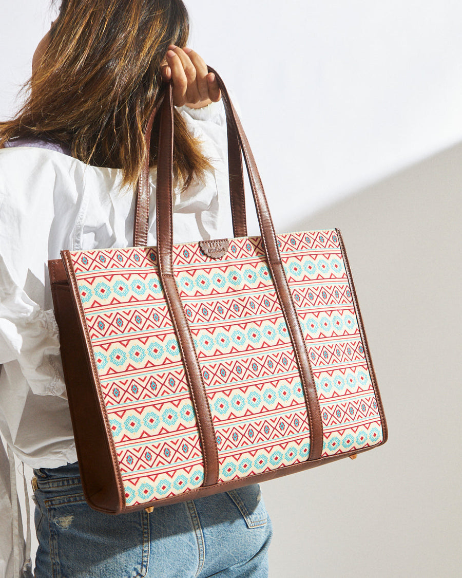 Woman carrying an Aztec pattern canvas tote bag with brown vegan leather handles, wearing white blouse and jeans