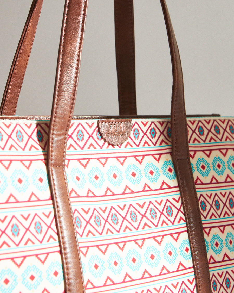 Close-up detail of the tote bag's patterned canvas with brown vegan leather strap and small decorative badge