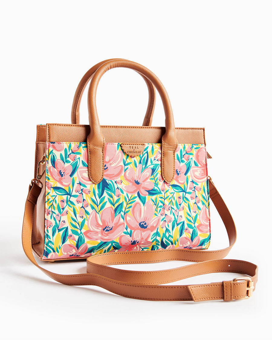 Tan leather handbag with pink floral fabric featuring large flowers and green foliage soft lighting