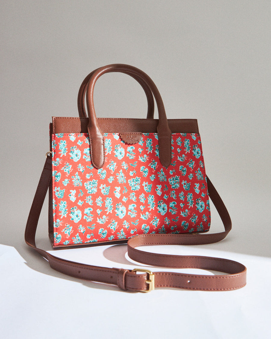 Brown leather handbag with coral fabric featuring delicate blue and white floral print and adjustable strap