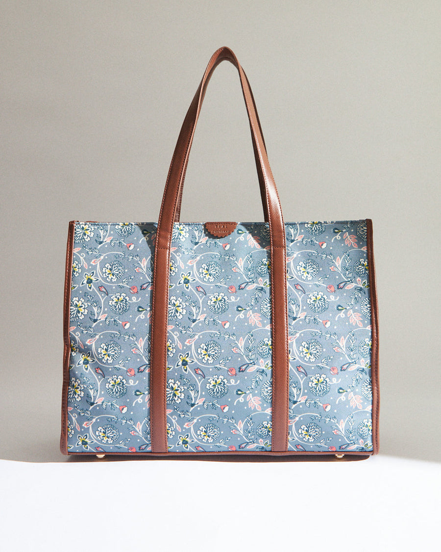 Blue canvas tote bag with white and pink floral pattern and brown leather handles and trim