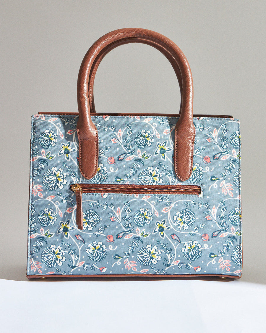 Back view of teal floral canvas handbag showing exterior zippered pocket and brown vegan leather handles