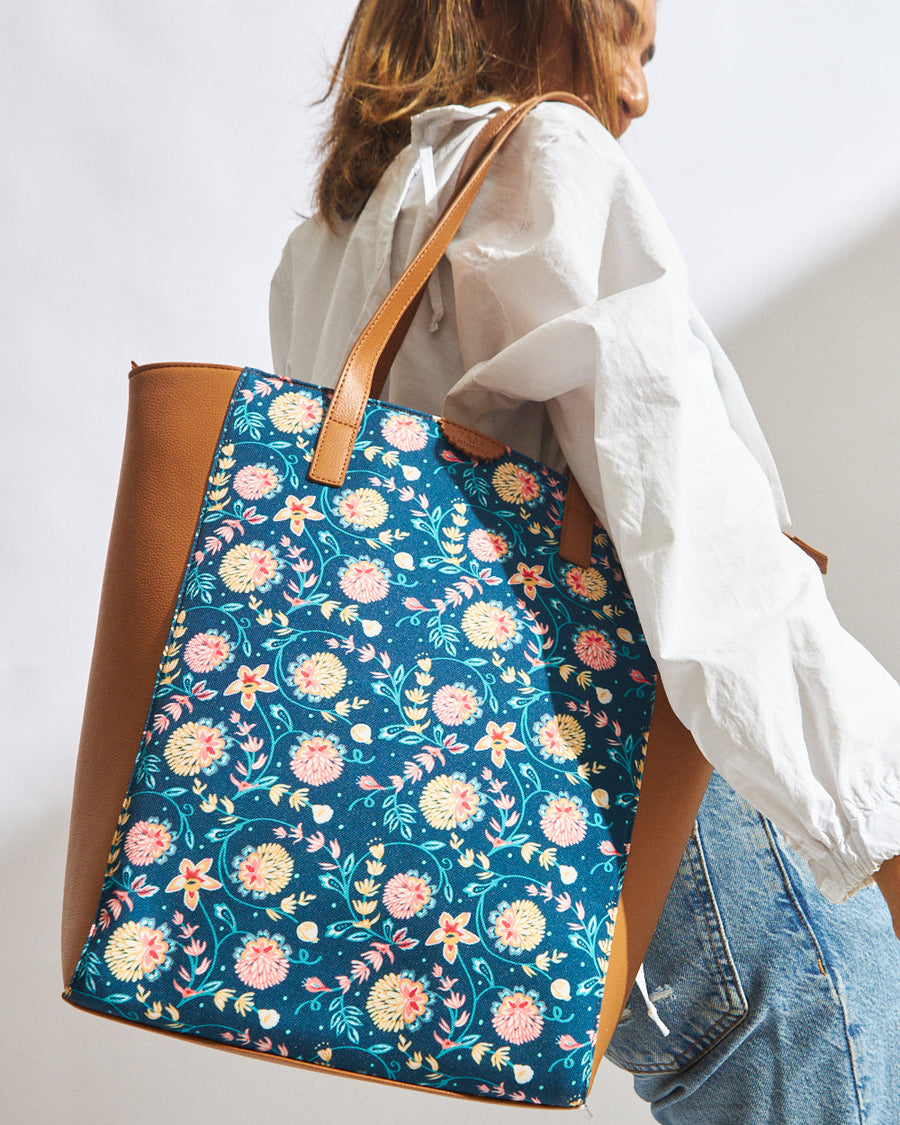 Woman carrying a blue floral canvas and tan vegan leather tote bag over shoulder