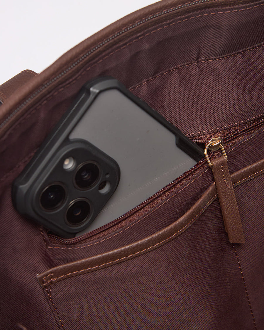 Close-up of interior pocket with phone partially inserted, showing brown linings and zipper pull