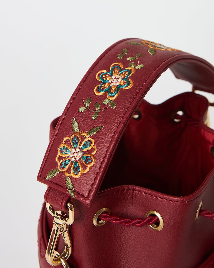 Close-up shot of floral embroidery on padded handle of red leather bucket bag