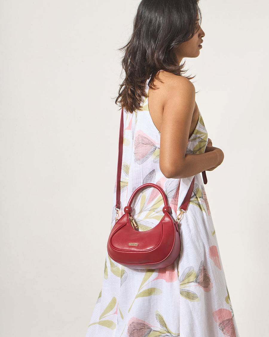 Side view of woman wearing the maroon vegan leather crescent handbag crossbody style with floral dress.