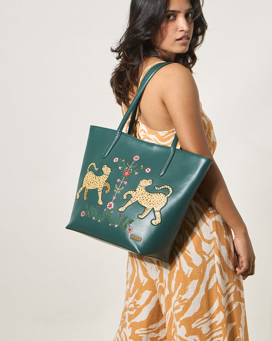 Woman wearing animal print dress carrying deep green embroidered tote bag on her shoulder against white background