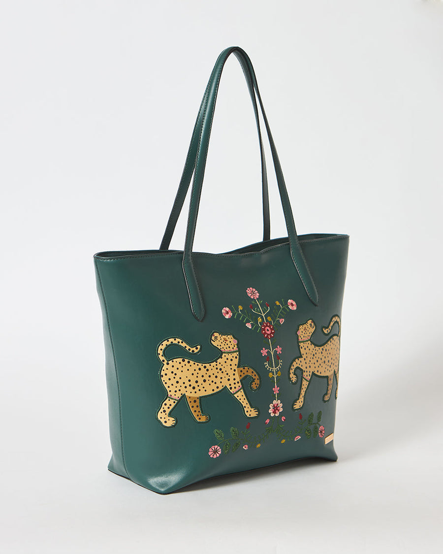Close-up of the detailed floral embroidery between two yellow leopard patches on the deep green tote bag