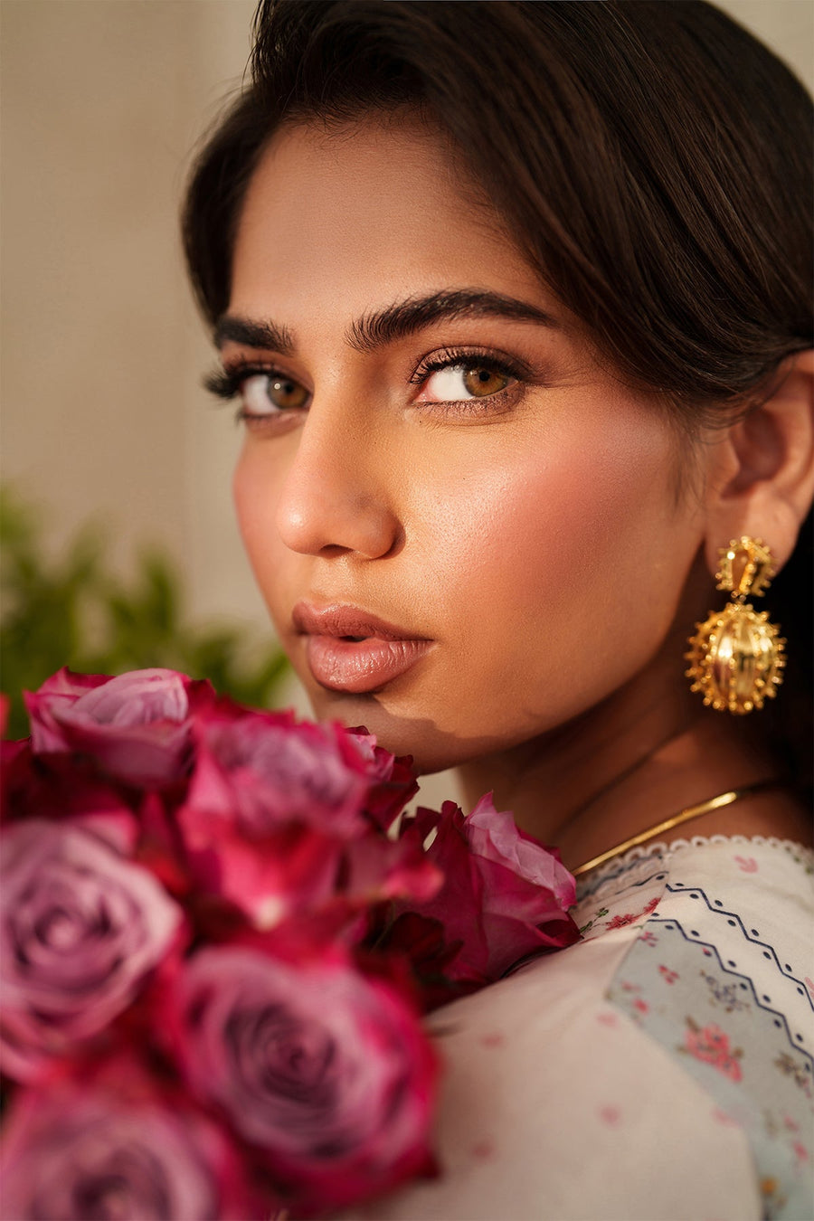 Close-up portrait of woman holding bouquet of pink roses wearing embroidered lawn suit and intricate gold earrings