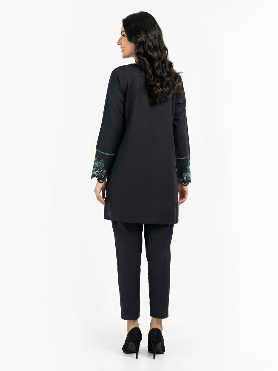 Back view of woman modeling plain black kurti and tapered trousers with scalloped embroidered sleeve cuffs