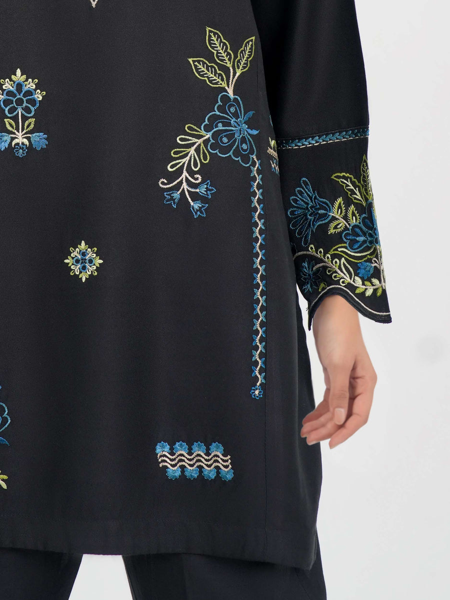 Detailed close-up of embroidery on black kurti sleeves and lower side seam showing scalloped edges and floral designs