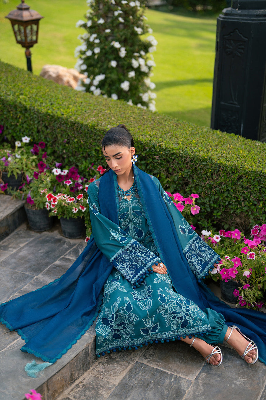 Woman sitting on steps wearing the three-piece suit highlighting embroidery, dupatta, and silver heels
