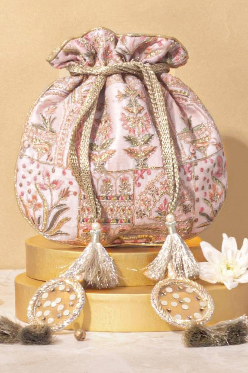 Soft pink embroidered potli bag with golden tassels placed on gold cylindrical stands and adorned with mirrored embellishments and pearls
