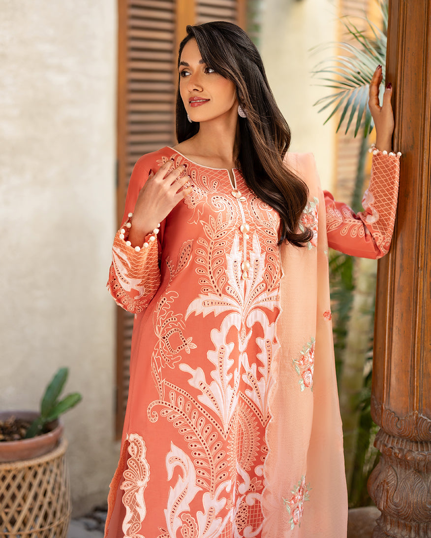 Close-up of the coral lawn shirt showing detailed white embroidery with pearl buttons and pom-pom cuffs, paired with peach net dupatta with floral embroidery.