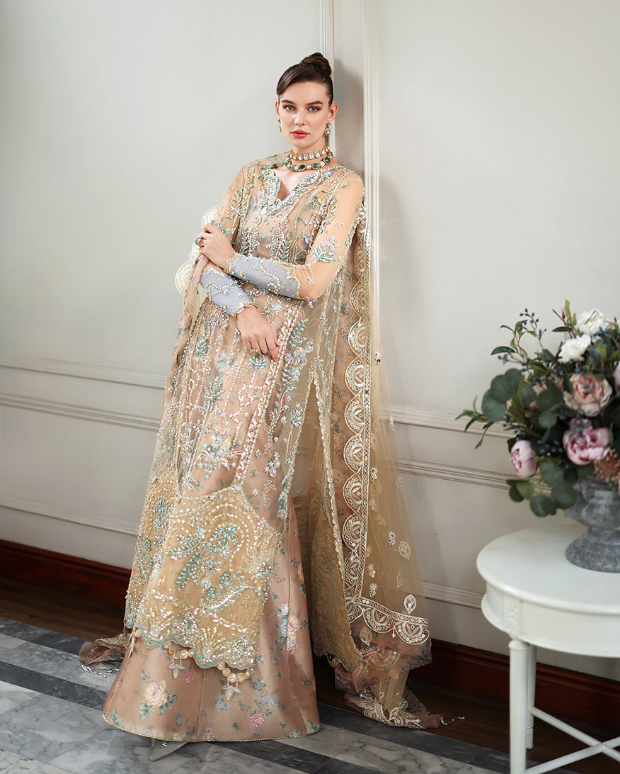 Full front view of woman in embellished net formal dress standing beside a floral arrangement, showcasing detailed embroidery and sequined sleeves